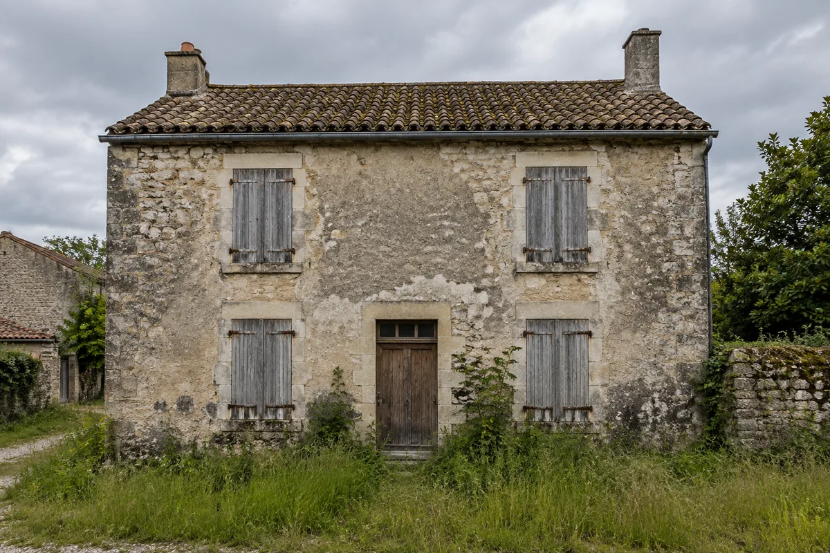 Maison ancienne à rénover aux volets fermés et à la façade marquée par l'humidité